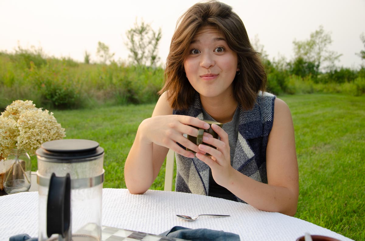 girl sitting at a table with a mug outside